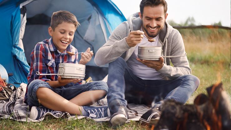 father and son eating at campfire