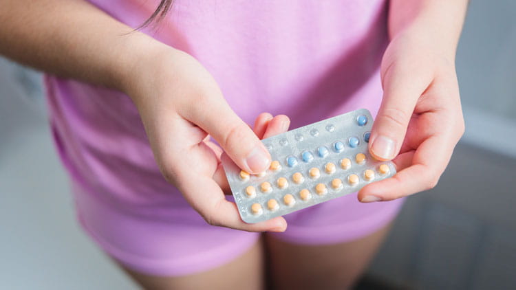 A young woman, dressed in a pink pajamas, holding her contraceptive pills.