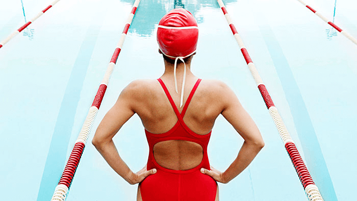 woman in swimsuit facing away from view standing at the edge of a pool