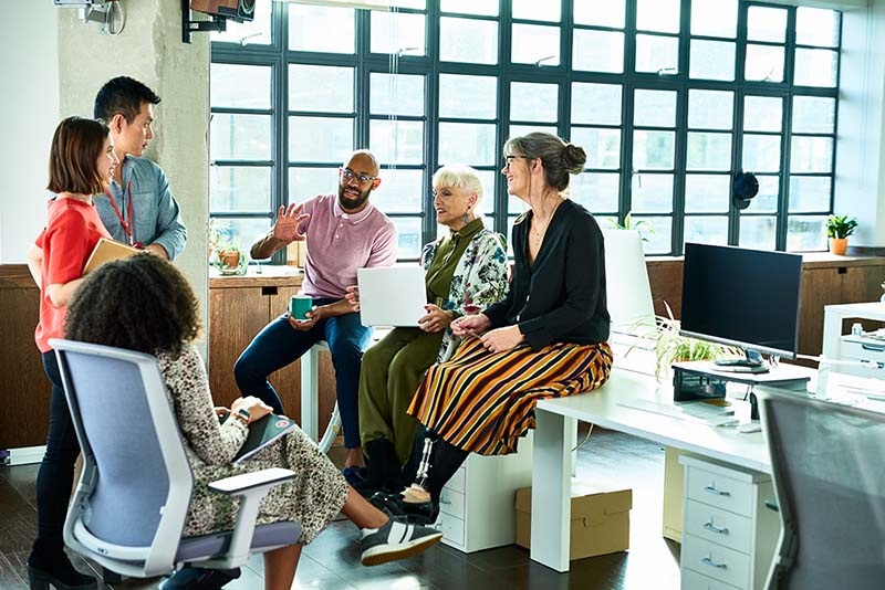 Group of employees gathered in office, casually sitting in chairs and on desks