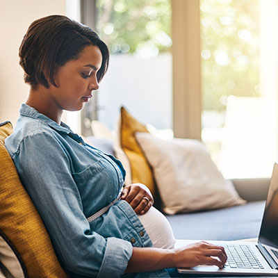 pregnant woman uses laptop on couch